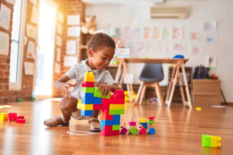 Beautiful african american toddler playing with building blocks smiling at kindergarten